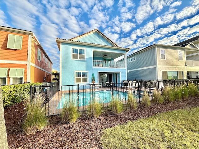 rear view of property with ceiling fan, a balcony, and a fenced in pool