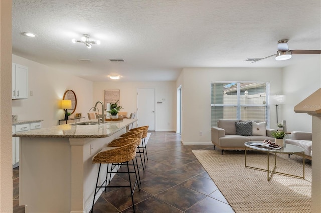 kitchen with a breakfast bar, white cabinetry, sink, a center island with sink, and a textured ceiling