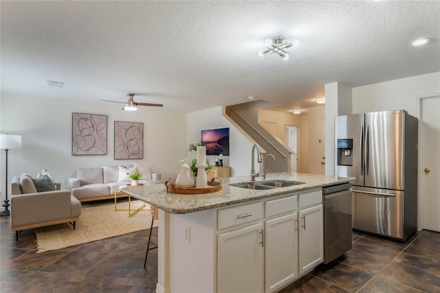 kitchen with sink, white cabinetry, light stone counters, a center island with sink, and stainless steel appliances