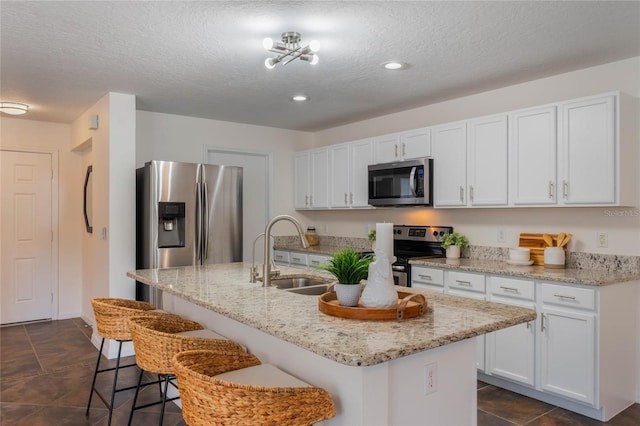 kitchen featuring appliances with stainless steel finishes, sink, white cabinets, a kitchen breakfast bar, and a center island with sink