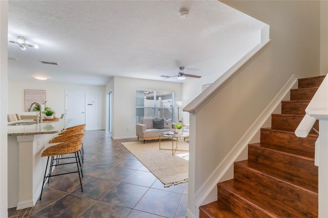 staircase with tile patterned flooring, ceiling fan, sink, and a textured ceiling