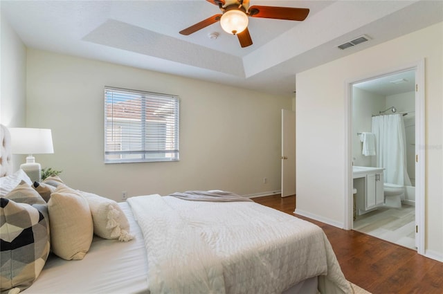 bedroom with ceiling fan, connected bathroom, a tray ceiling, and light hardwood / wood-style floors