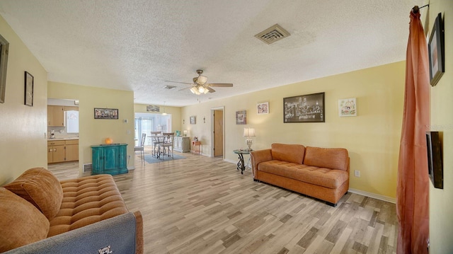 living room with a textured ceiling, ceiling fan, and light hardwood / wood-style floors