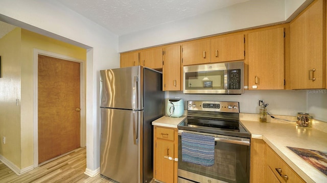 kitchen featuring a textured ceiling, light hardwood / wood-style flooring, and stainless steel appliances