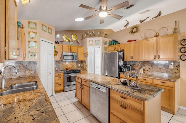 kitchen with appliances with stainless steel finishes, light stone counters, a kitchen island, and sink