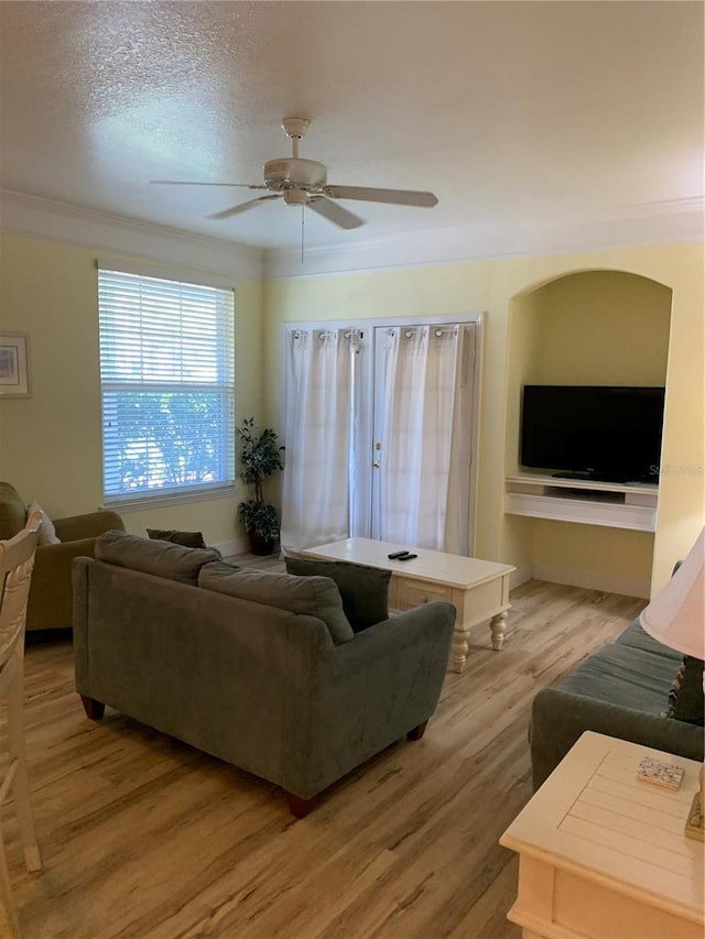 living room featuring ceiling fan, ornamental molding, a textured ceiling, and light hardwood / wood-style flooring