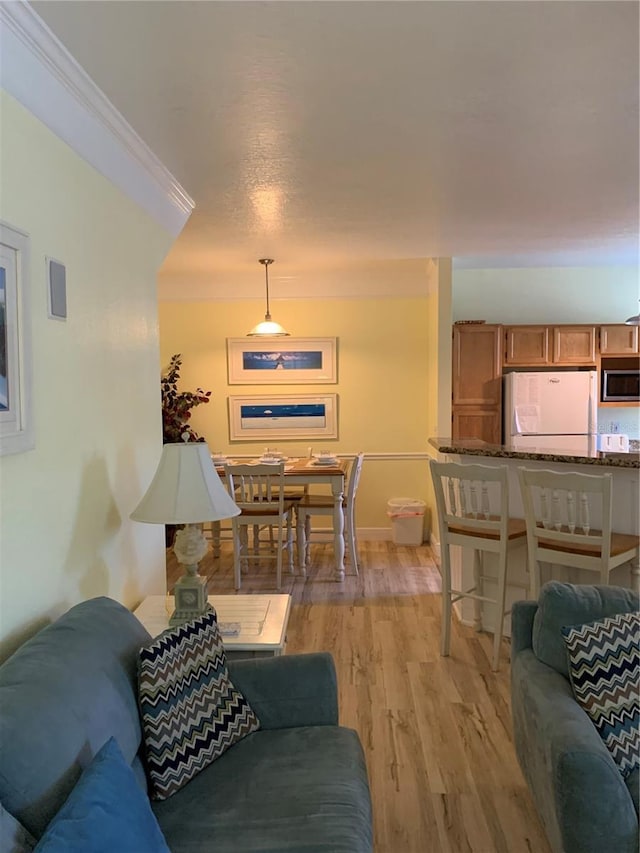 living area with light wood-type flooring, crown molding, and baseboards