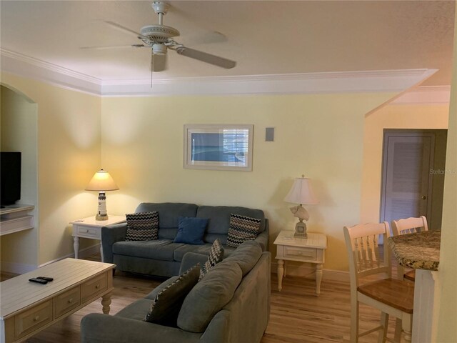 living room featuring arched walkways, crown molding, light wood-style floors, a ceiling fan, and baseboards
