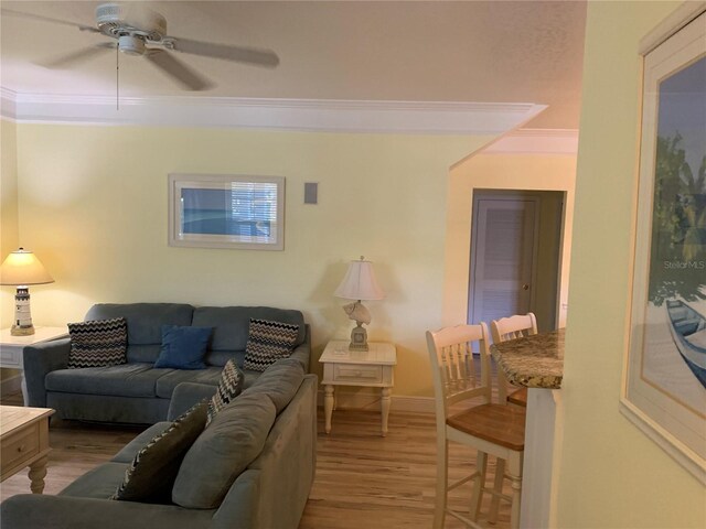 living area with baseboards, a ceiling fan, crown molding, and wood finished floors