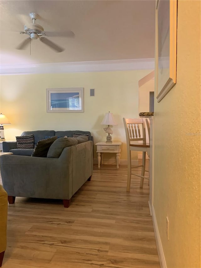 living area with baseboards, wood finished floors, a ceiling fan, and crown molding