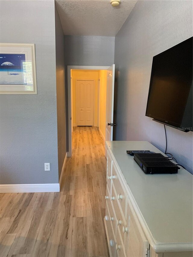 hall with light wood-type flooring, a textured ceiling, and baseboards
