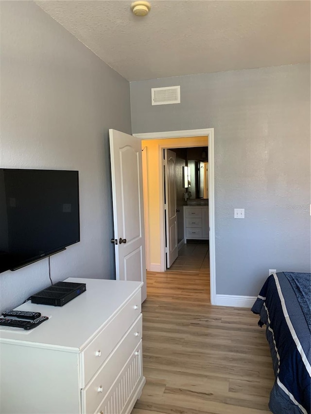 bedroom with a textured ceiling, light wood-type flooring, visible vents, and baseboards