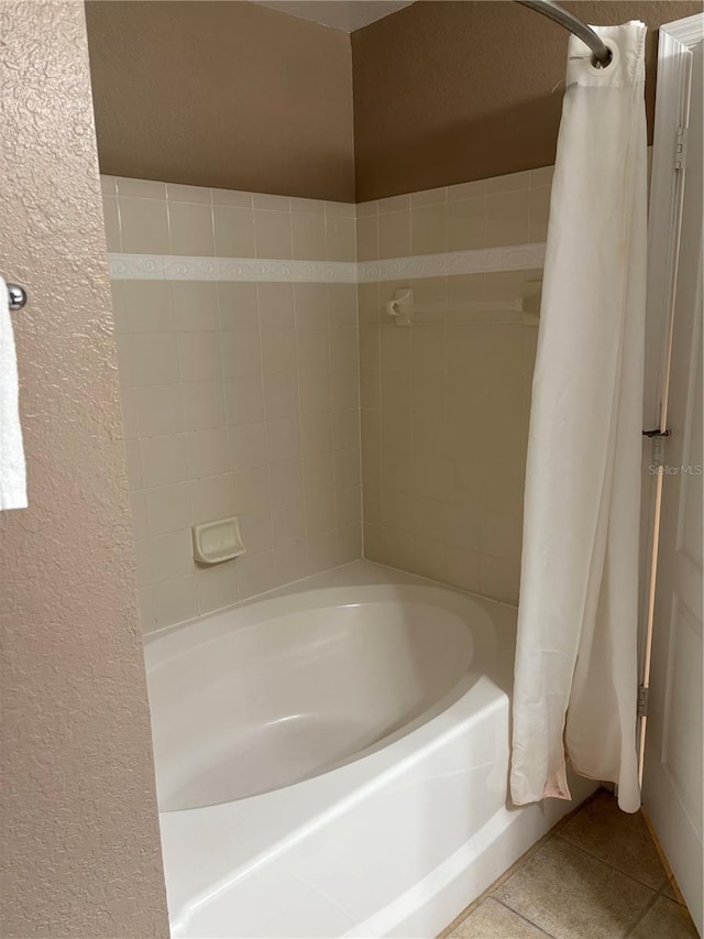 bathroom featuring a textured wall, shower / bath combo with shower curtain, and tile patterned floors