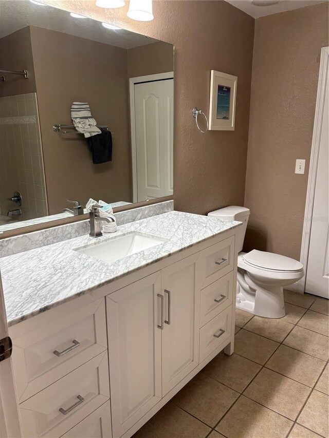 bathroom with a textured wall, tile patterned flooring, toilet, vanity, and a closet
