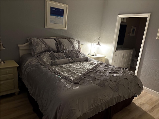 bedroom with connected bathroom, baseboards, wood finished floors, and a textured wall