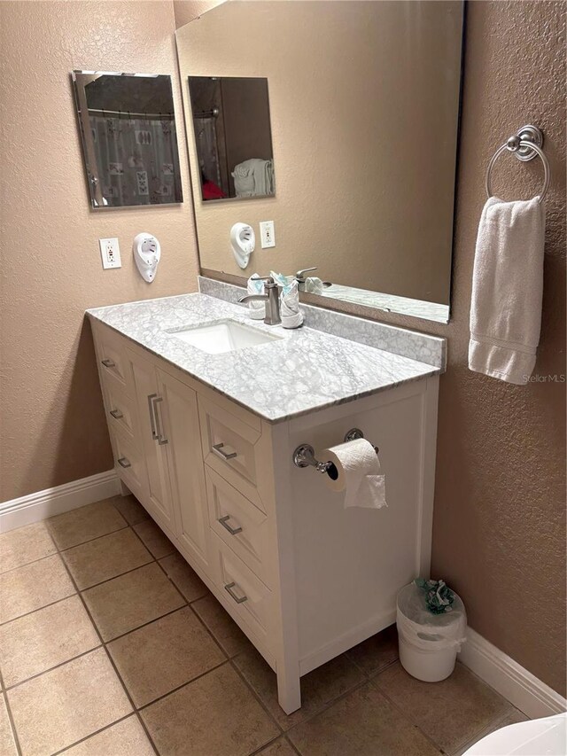 bathroom featuring baseboards, a textured wall, vanity, and tile patterned floors
