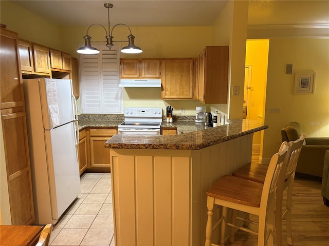 kitchen featuring light tile patterned floors, a breakfast bar area, under cabinet range hood, a peninsula, and white appliances