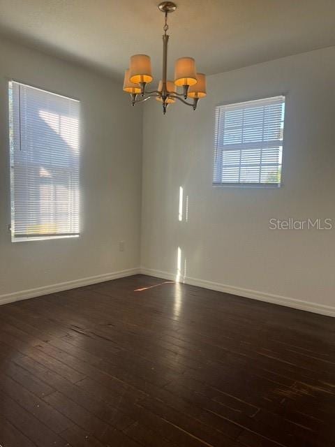 spare room with a healthy amount of sunlight, dark wood-type flooring, and a chandelier