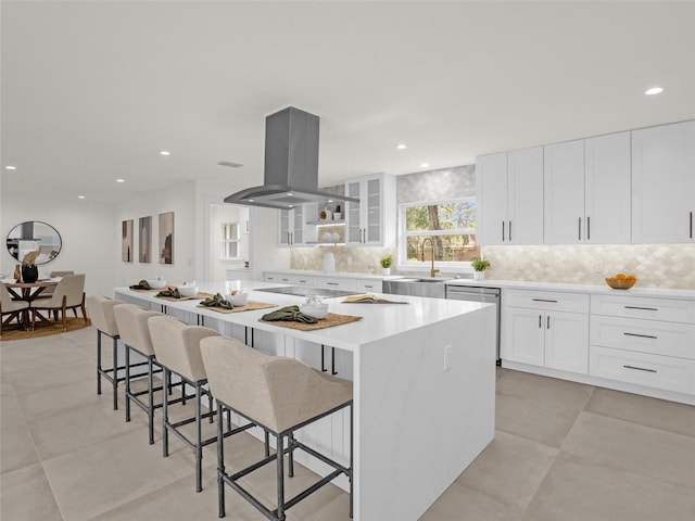 kitchen featuring a kitchen breakfast bar, island range hood, sink, white cabinets, and a kitchen island