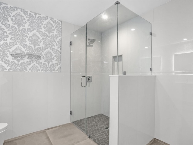 bathroom with toilet, tile walls, and a shower with shower door