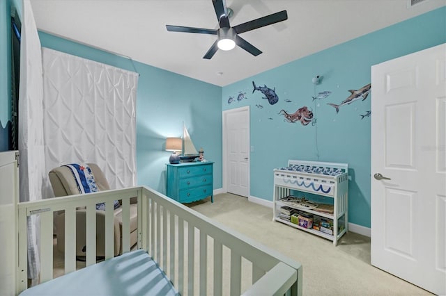 bedroom with a nursery area, a ceiling fan, baseboards, and carpet flooring