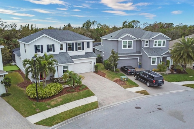 traditional-style home featuring decorative driveway, an attached garage, a front yard, and stucco siding