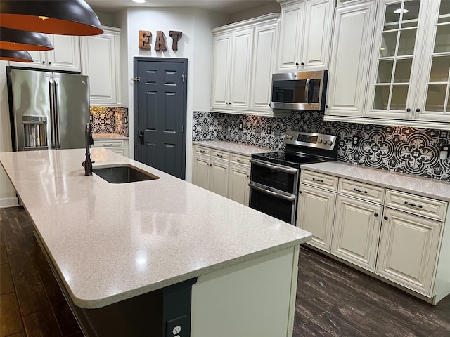 kitchen with a kitchen island with sink, stainless steel appliances, a sink, dark wood-style floors, and glass insert cabinets