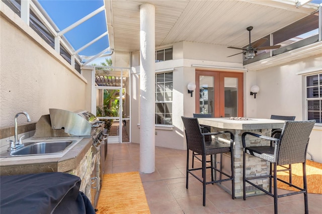 view of patio with glass enclosure, ceiling fan, exterior kitchen, and a wet bar