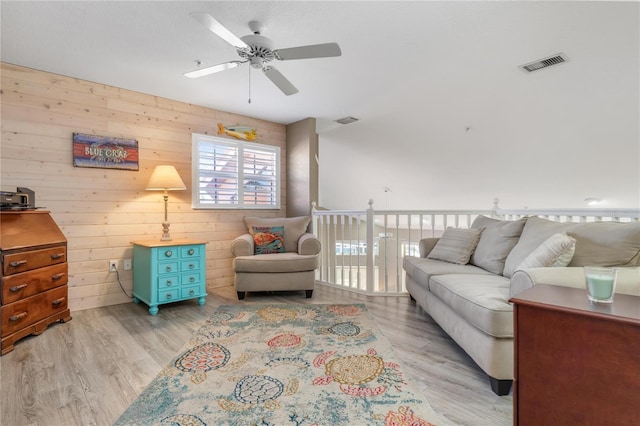 living room with light hardwood / wood-style floors, ceiling fan, and wood walls