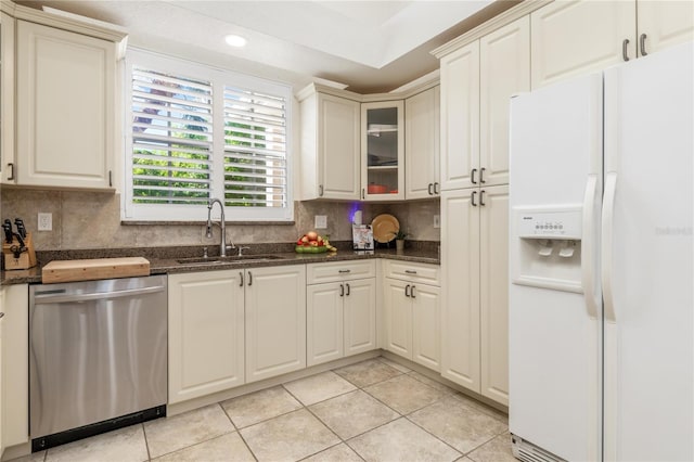 kitchen with stainless steel dishwasher, dark stone counters, sink, white refrigerator with ice dispenser, and light tile patterned floors