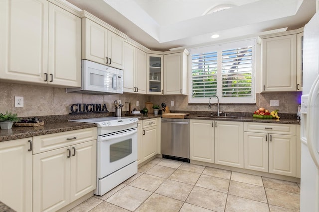 kitchen featuring decorative backsplash, white appliances, sink, light tile patterned floors, and dark stone countertops