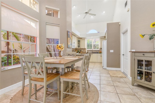 tiled dining space featuring ceiling fan, sink, and a high ceiling