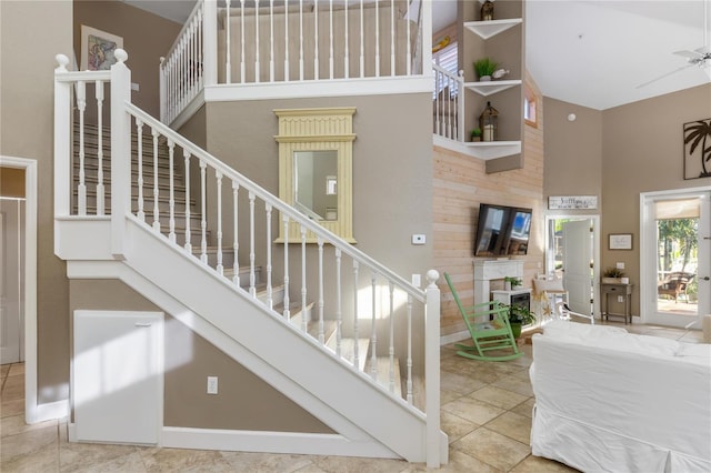 stairway with tile patterned flooring, ceiling fan, and a towering ceiling