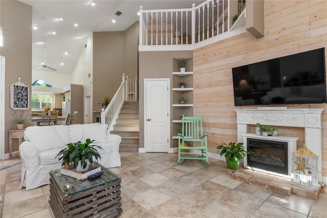 living room with ceiling fan, wood walls, a high ceiling, and built in shelves