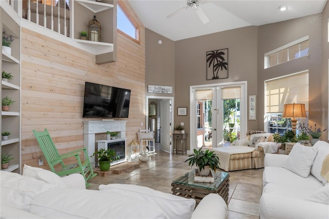 living room with wooden walls, ceiling fan, a high ceiling, and french doors