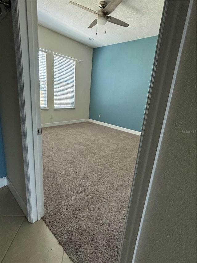 interior space with light carpet, ceiling fan, a textured ceiling, and baseboards