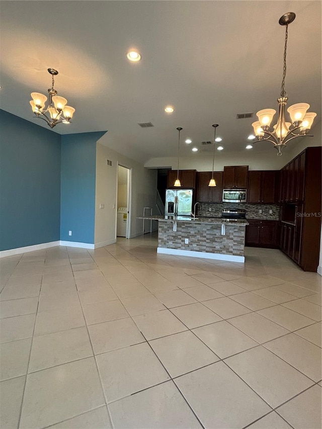 kitchen with a chandelier, light tile patterned floors, open floor plan, appliances with stainless steel finishes, and backsplash