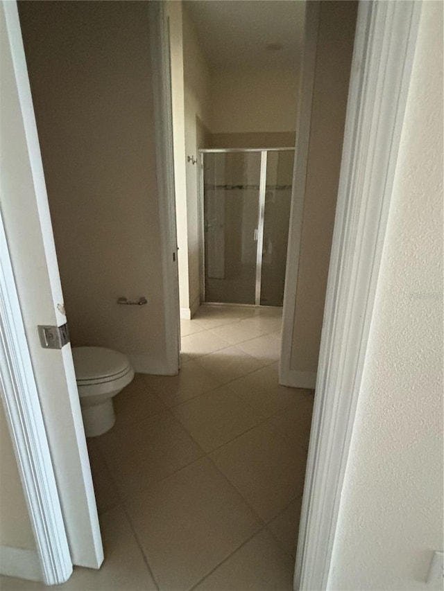 bathroom featuring tile patterned flooring, a shower with shower door, and toilet