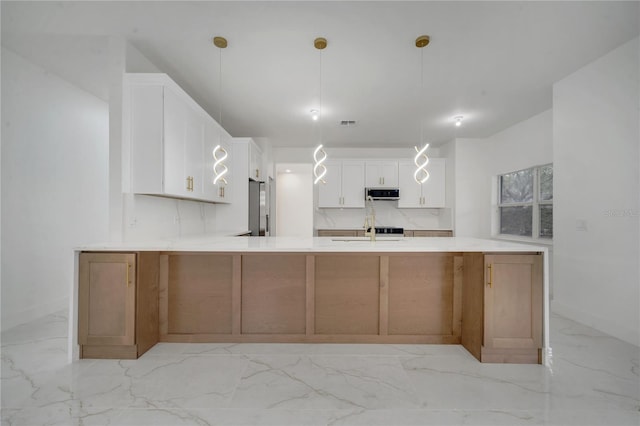 kitchen with white cabinetry, kitchen peninsula, stainless steel fridge, backsplash, and hanging light fixtures