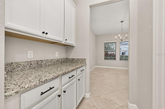 kitchen featuring white cabinets, an inviting chandelier, light stone countertops, and light tile patterned flooring