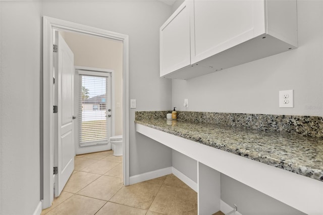 kitchen featuring white cabinetry, light stone counters, light tile patterned flooring, and built in desk