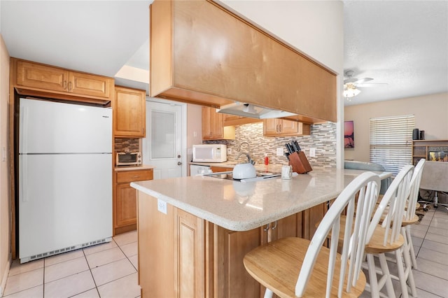 kitchen featuring a breakfast bar, white appliances, backsplash, ceiling fan, and kitchen peninsula