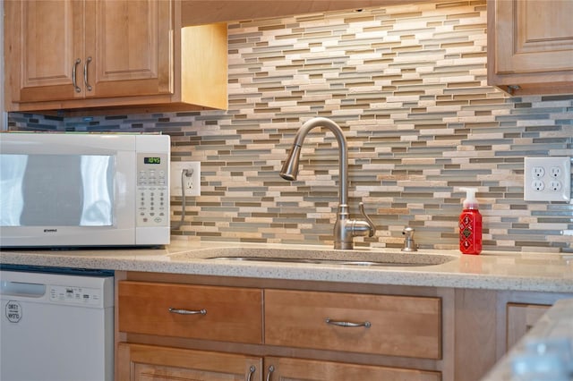 kitchen featuring decorative backsplash, white appliances, light stone counters, and sink