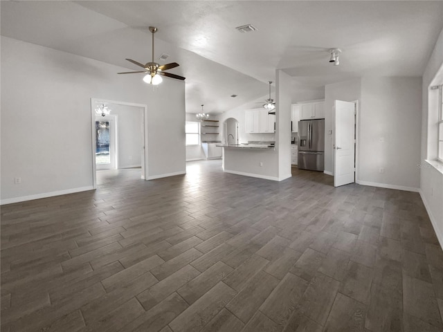 unfurnished living room featuring ceiling fan with notable chandelier and vaulted ceiling