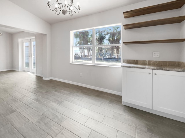 unfurnished dining area featuring an inviting chandelier, vaulted ceiling, and french doors