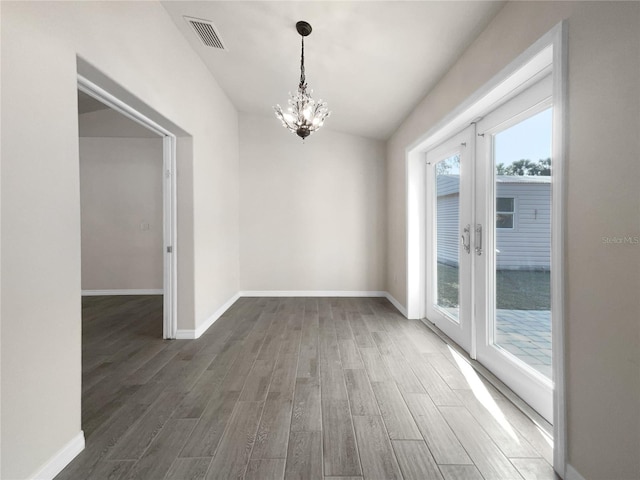 unfurnished dining area with dark hardwood / wood-style flooring, french doors, and a notable chandelier