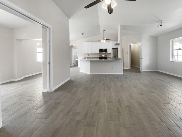 unfurnished living room featuring ceiling fan, wood-type flooring, a wealth of natural light, and vaulted ceiling