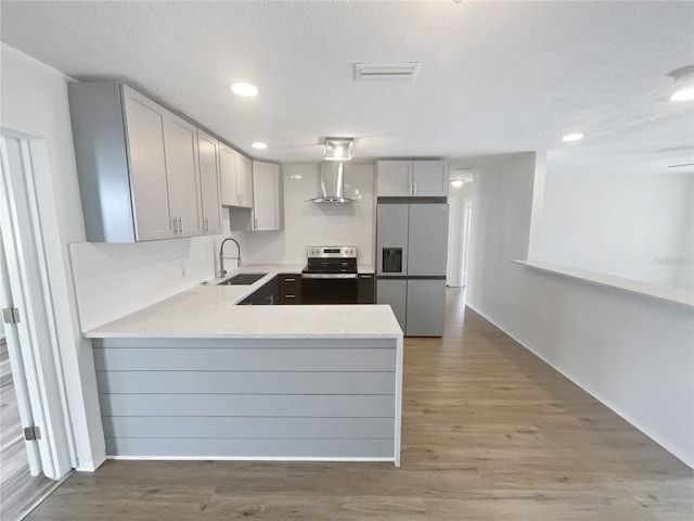 kitchen with sink, wall chimney exhaust hood, kitchen peninsula, appliances with stainless steel finishes, and hardwood / wood-style flooring