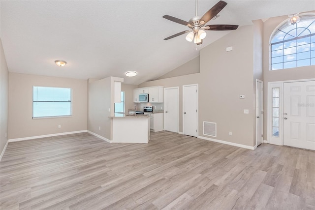 unfurnished living room with a towering ceiling, light wood-type flooring, a textured ceiling, and ceiling fan