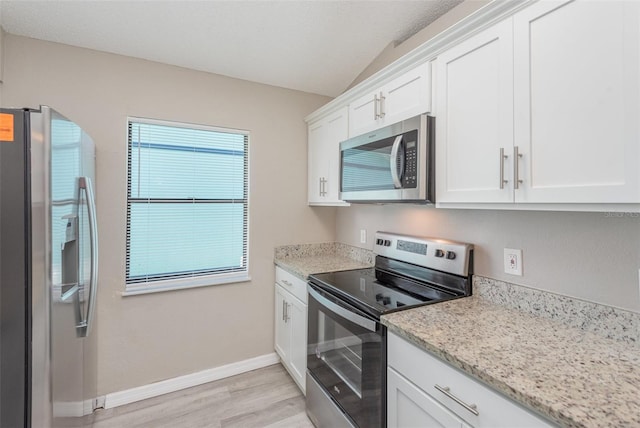 kitchen with lofted ceiling, white cabinets, light hardwood / wood-style flooring, appliances with stainless steel finishes, and light stone counters